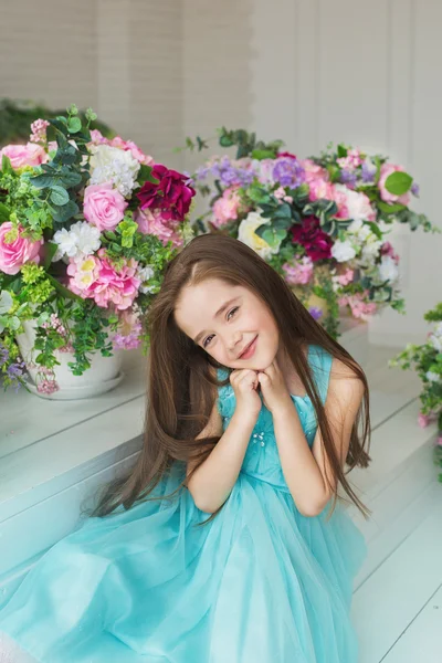 Portrait of a smiling pretty little girl in a turquoise dress in a studio decorated a flowers