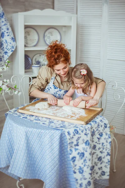 Young mother help to roll a dough to her little daughter