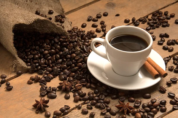 Coffee cup with coffee beans, cinnamon  on bagging and wood.