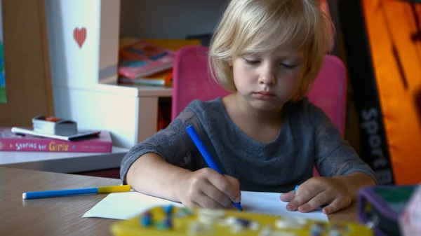 A child with long blond hair is painting something with markers pens, looking away