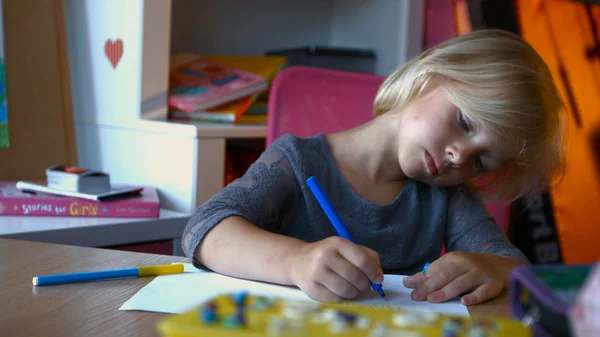 A child with long blond hair is painting something with markers pens, looking away