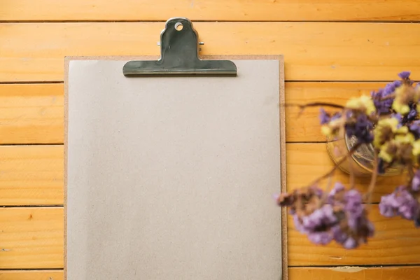 Clipboard with Blank Paper and flower on wooden Table. Top View