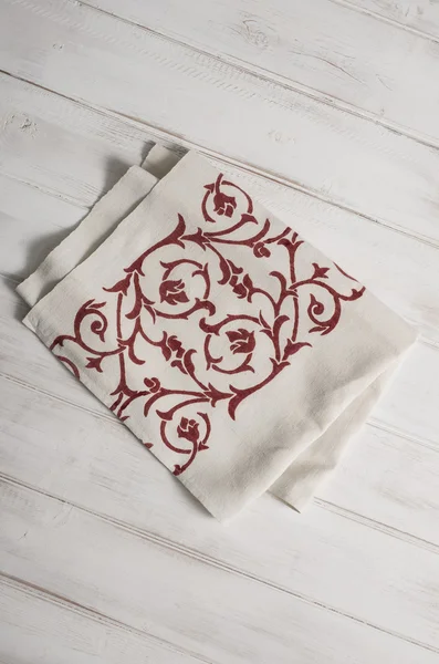 White Dinner Napkin with Red Floral Pattern on Wooden Surface