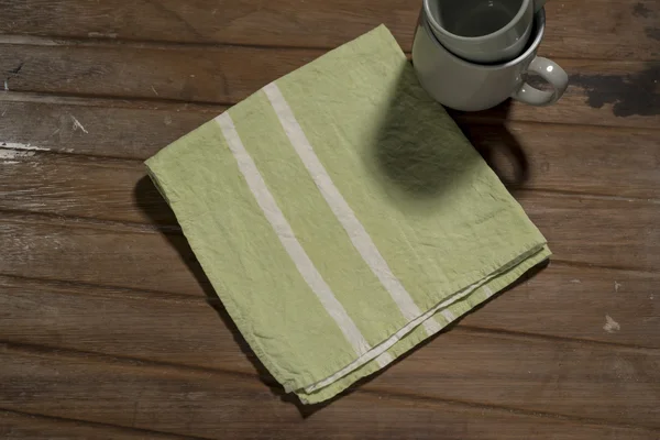 Green Dinner Napkin with White Bands Alongside Stack of Cups