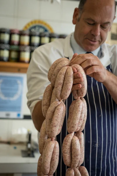 Male butcher in blue apron holding sausages