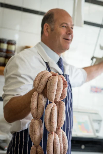 Smiling butcher holding up a string of sausages