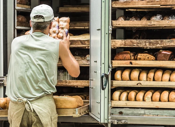 Shelves full of various bread. Man takes them