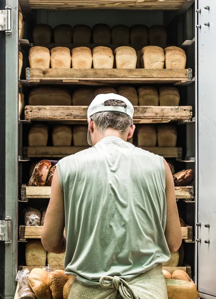 Shelves full of various bread. Man takes them