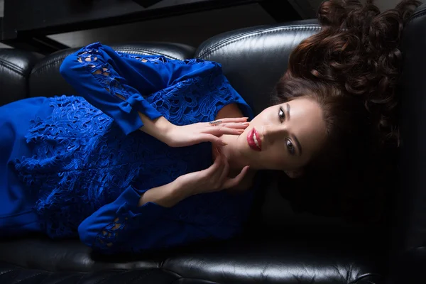 Young beautiful brunette girl lies on a leather couch.