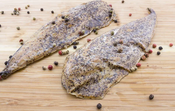 Two peppered, mustard encrusted smoked mackerel on wood cutting