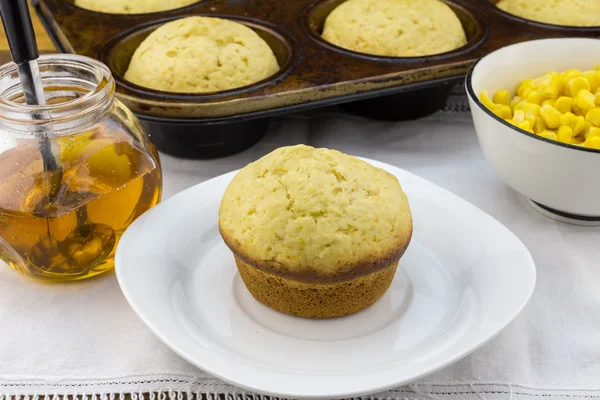 Corn muffin in plate with muffins in pan, syrup and corn in a bowl