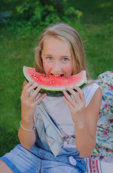 Cute young girl eating  water-melon on the grass in summertime