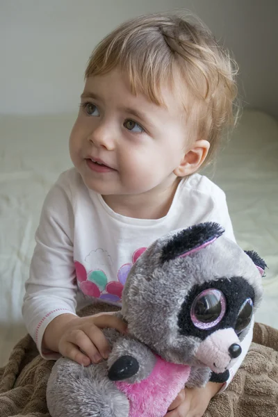 Clouse-up portrait small child sitting on the bed in the room hugging a stuffed toy lemur