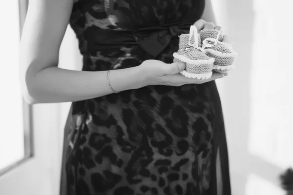 Closeup black and white photo of pregnant woman showing baby shoes