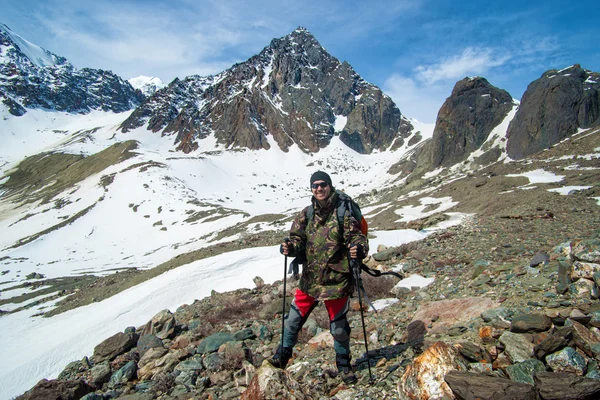 Hiker man on the summit with trekking poles. Snowy mountain land