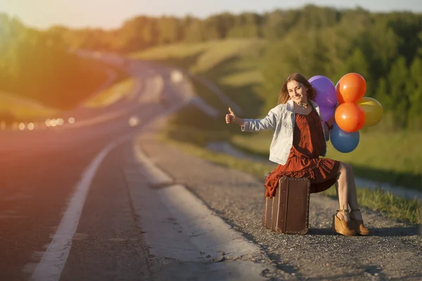Happy young woman with balloons and large suitcase walking along