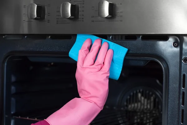Woman hand in protective glove with rag cleaning oven at home ki