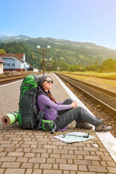 Girl with backpack and map waiting train at the railway station