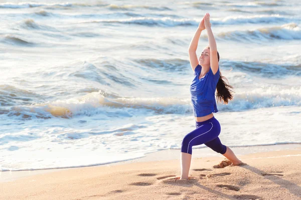 Woman practicing yoga warrior position on the beach