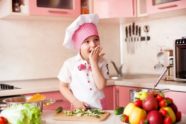 Portrait of little boy in the hat of the chef and an apron. Little chef cooks in the kitchen.