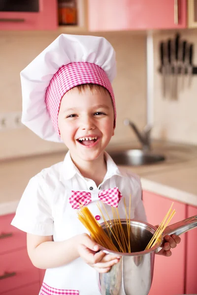 Portrait of little boy in the hat of the chef and an apron. Little cooks chef in the kitchen preparing spaghetti. Emotional pictures