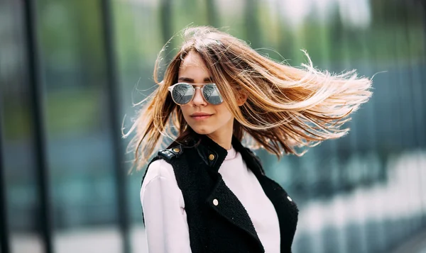 Young beautiful model in the city. Beautiful blond woman wearing sunglasses. Dynamically young girl walks down the street.Hair fluttering in the wind.