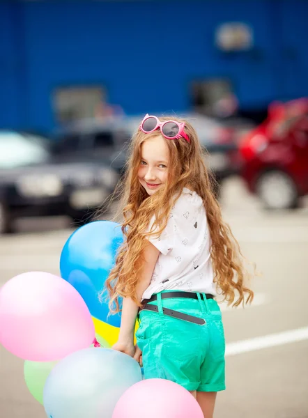 Little girl in bright clothes playing with balloons. Happy kid playing with colorful balloons.