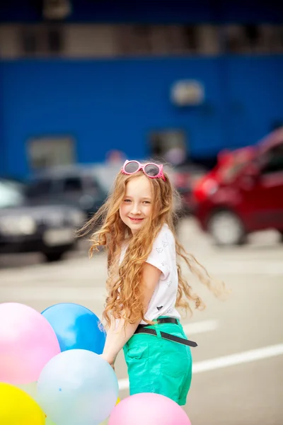 Little girl in bright clothes playing with balloons. Happy kid playing with colorful balloons.