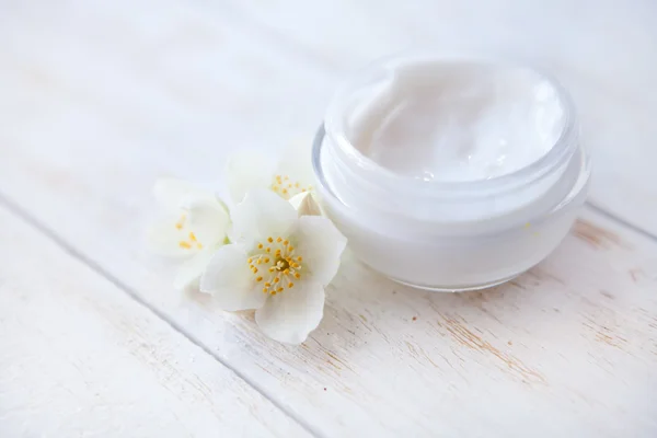 Face cream with jasmine blossom on white wooden table