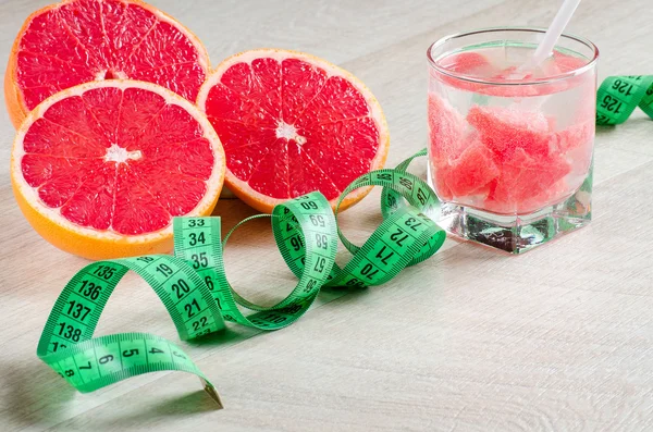Red grapefruit, drink and a measuring tape on the table