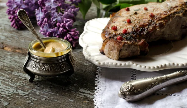 Pork steak, mustard in a jar on the table. Vintage style.