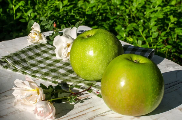 Two green apples and roses on the table in the garden