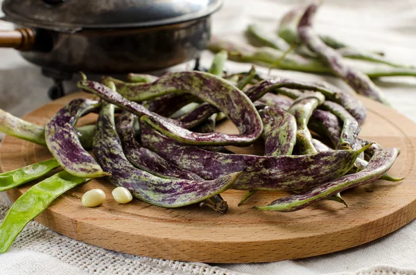 Purple speckled kidney beans with pods on wooden round Board