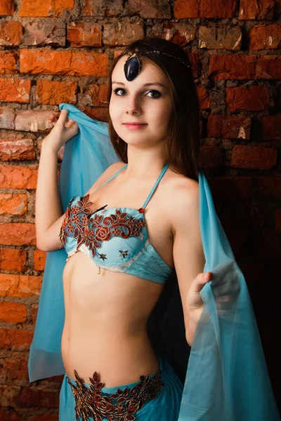 Beautiful young brunette in a blue suit oriental dance over a br