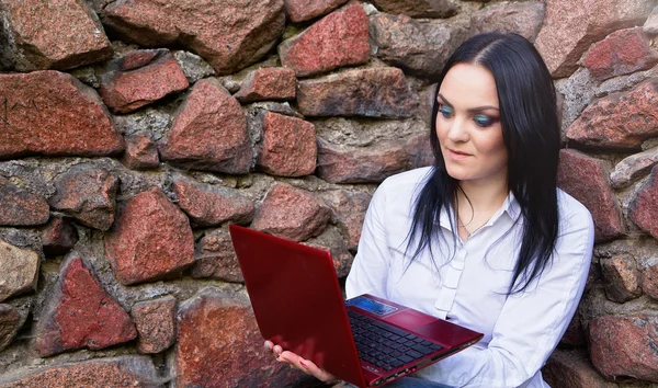 Beautiful business woman sitting with laptop over a stone wall