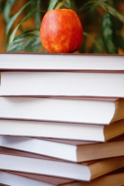 Stack of books on wooden table for reading with red delicious ap