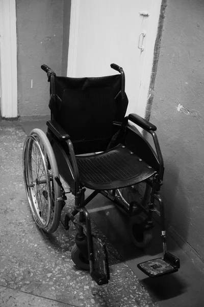 Old wheelchair standing in a empty corridor. Black and white pho