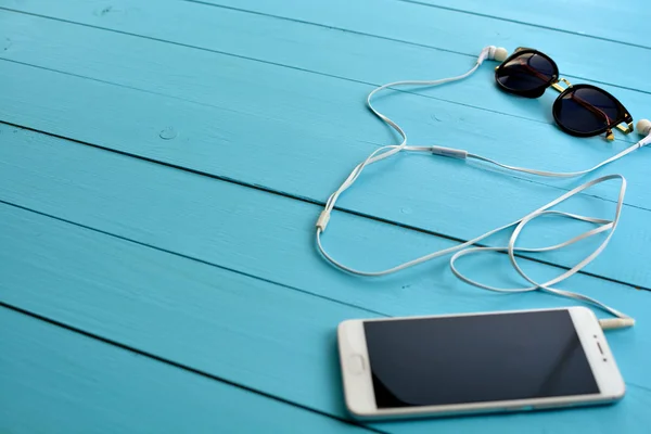 Cell phone and headphones on a blue wooden table.