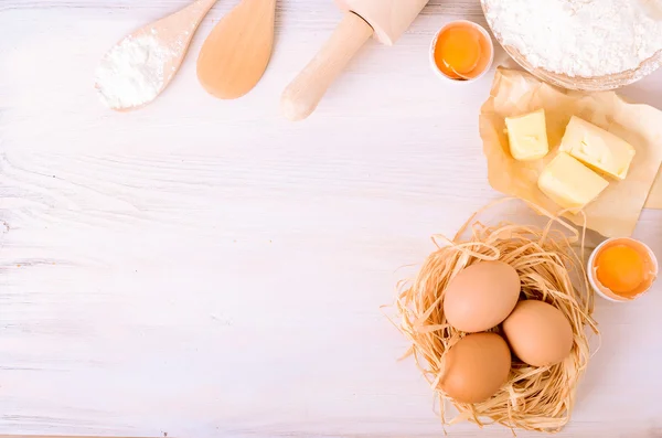 Ingredients for baking croissants - paper, flour, wooden spoon, rolling pin, eggs, egg yolks, butter served on white background.