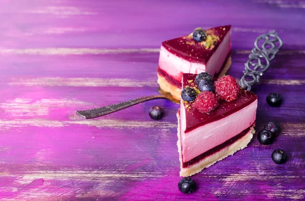 Piece of delicious raspberry cake with fresh raspberries, blueberry, currants and pistachios on shovel, bright purple, violet background. Free space for your text.