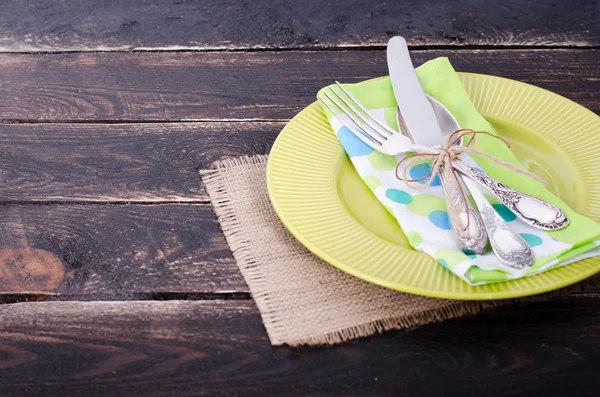 Green plate, napkin, knife, fork on wooden background. Free space for your text.