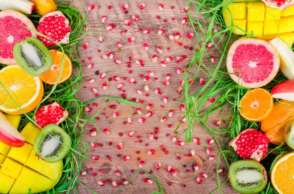 Fresh fruits on grass and wooden background. Raw and vegetarian eating frame. Sliced orange, persimmon, kiwi, tangerine, banana, lemon, apple,  grapefruit, pomegranate, lime, mango. Fruit set.