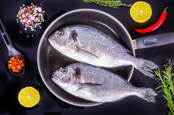 Fresh raw gilthead fishes with lemon, herbs, salt on black background. Healthy food concept. Food frame