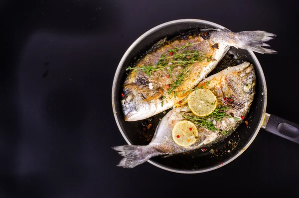 Roasted gilthead fishes with lemon, herbs, salt on black background. Healthy food concept. Food frame. Free space for your text.