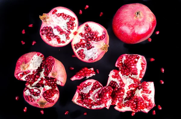 Red juicy pomegranate, whole , half, ripe and broken fruits on black background.