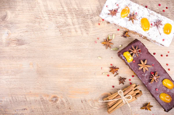 Chocolate spices cake with star anise and dried fruits, cinnamon, cloves, cardamom, handmade milk chocolate with nuts on wooden background. Christmas gift.