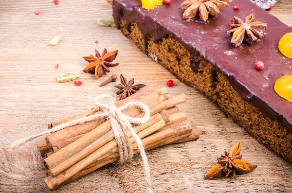 Chocolate spices cake with star anise and dried fruits, cinnamon, cloves, cardamom on wooden background. Christmas gift.