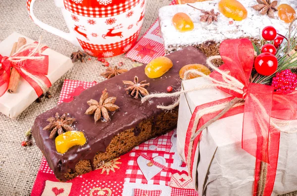 Chocolate spices cake, star anise and dried fruits, packed gifts with red tapes on sackcloth, canvas. Sweet frame. Top view