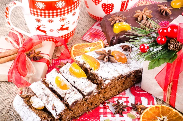 Chocolate spices cake, star anise and dried fruits, packed gifts with red tapes on sackcloth, canvas. Sweet frame. Top view