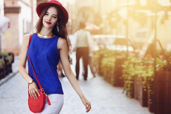 Outdoor portrait of young beautiful happy smiling woman posing on street. Model wearing stylish hat and clothes. Girl looking at camera. Female fashion. Sunny day. City lifestyle. Copy space for text